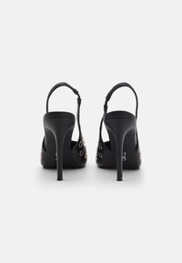 Chaussures à talons aiguilles noires à bride arrière avec une finition en cuir lisse, présentant des accents en œillets dorés et des talons fins.