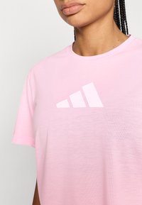 Rosa Sport-T-Shirt aus leichtem Stoff, mit weißem Adidas-Logo und drei Streifen über der Brust. Kurze Ärmel, rundhalsausschnitt.