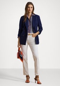 Navy pinstriped double-breasted blazer over a striped shirt, white jeans, and orange strappy heels. Accessories include a small red bag.