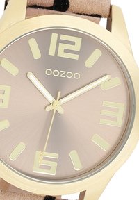 Gold-tone watch with a round face, light brown metallic dial, bold yellow markers, and a beige strap featuring black accents.