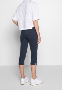 Camisa blanca corta de manga corta, combinada con pantalones azul marino hasta el tobillo con aberturas laterales. La modelo lleva zapatillas blancas.