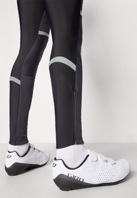 Fekete sport leggings reflektáló szürke részletekkel és alsó cipzárral. Fehér kerékpáros cipők hálós díszítéssel és fekete talppal.