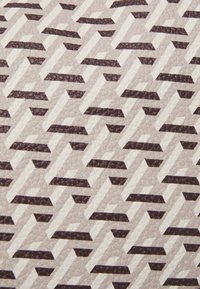 Texturovaný materiál s opakujícím se geometrickým vzorem proplétajících se tvarů v tmavě hnědé a krémové barvě na světle béžovém pozadí.