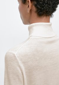 Roomkleurige coltrui gemaakt van zachte stof, met een getailleerd ontwerp, geribbelde kraag en subtiele gebreide textuur.