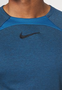 Camiseta deportiva Nike azul con cuello redondo, tejido con textura y logotipo negro en el pecho. Detalles de diseño sutiles en azul contrastante.