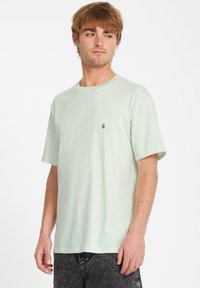 Lys grøn bomuld t-shirt med korte ærmer, rund hals og lille lilla logo på venstre bryst. Blød tekstur og afslappet pasform.