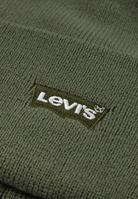 Olijfgroene gebreide beanie met een geribbelde textuur en een rechthoekig, geborduurd Levi's-logo in wit en donkergroen op een patch.
