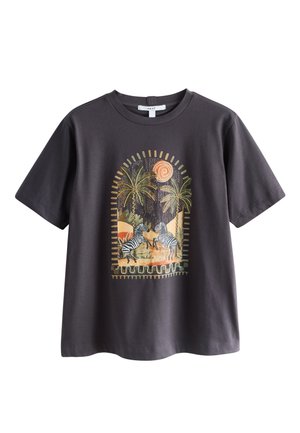 Kvinde med langt mørkt hår iført en sort t-shirt med zebraer og palmer design samt optrukne denimshorts foran en tekstureret væg.