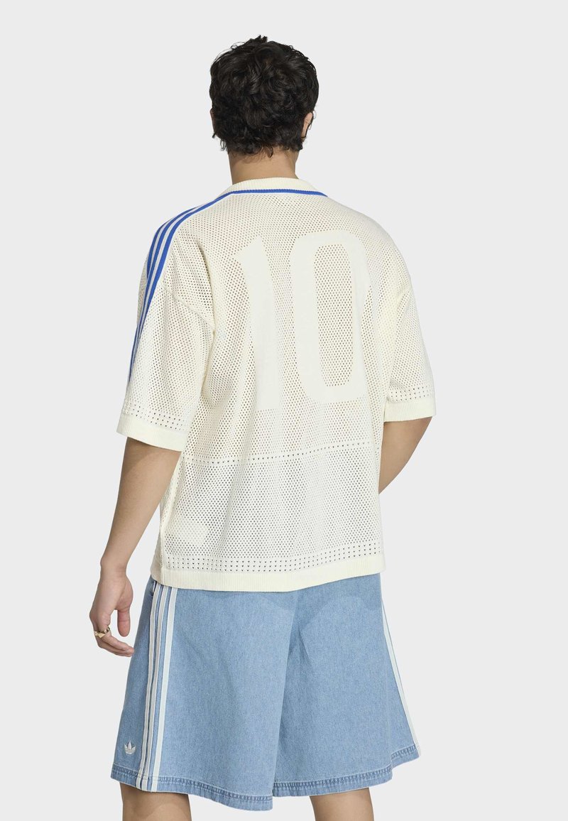 Persoon die een wit sportshirt met mesh en nummer 10 draagt, met licht denim shorts met blauwe strepen, van achteren gezien tegen een effen achtergrond.