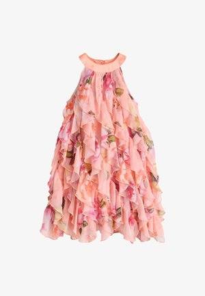 Niña vestida con un vestido rosa con flores, sin mangas y con volantes, y zapatos planos dorados tejidos, sobre un fondo liso y claro.