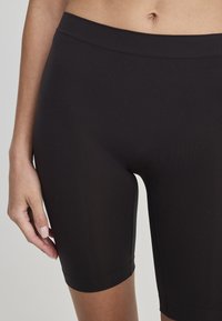 Czarne szorty rowerowe z elastycznego materiału o smukłym kroju, długości do połowy uda, z gładką talią. Materiał wydaje się lekki i ma delikatny połysk.