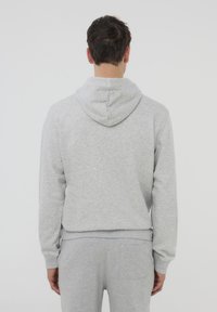 Felpa leggera grigia realizzata in un materiale morbido con un cappuccio curvo, polsini a coste e un design pulito e minimalista. Vista posteriore mostrata.