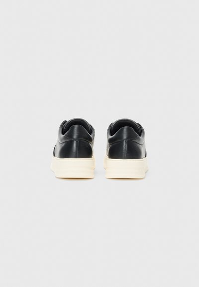 Black leather sneakers with a smooth finish, featuring a contrasting white rubber sole. Rounded shape, minimalistic design, no visible hardware.
