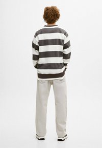 Sudadera a rayas en gris y blanco, con cuello y puños acanalados, combinada con pantalones de corte relajado en color claro y zapatillas deportivas.