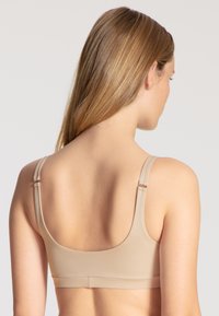 Beige nahtloser BH mit breiten Trägern, glatter Textur und minimalem Zubehör. Verfügt über ein abgerundetes Rückendesign und verstellbare Trageoptionen.