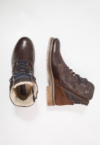 Braune Leder-Ankle-Boots mit einem mit Schaffell gefütterten Schaft und einer robusten Gummisohle. Das Design umfasst blaue Schnürsenkel und einen seitlichen Reißverschluss.