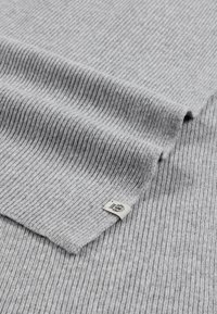 Light gray ribbed knit fabric with a small rectangular tag featuring a black emblem near the folded edge.