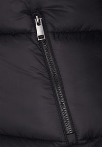 Schwarzer gepolsterter Stoff mit einem vertikalen schwarzen Plastikreißverschluss, der einen silbernen Metall-Zuglasche hat und teilweise geschlossen ist.