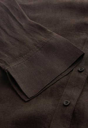 Barna len ing sima textúrával, gombos elülső résszel, hosszú ujjal és hajtott mandzsetta részlettel. A dizájnt fekete gombok díszítik.