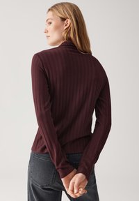 Top lungo a maniche lunghe bordeaux a coste con collo alto, featuring maniche aderenti e una texture liscia. La vista posteriore mostra un design semplice e lineare.