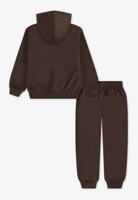 Hanorac cu capuz de culoare maro, cu tiv și manșete elastice, asortat cu pantaloni de trening cu talie elastică, toate dintr-un material moale și neted.