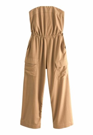 Tan, strapless jumpsuit met een relaxed fit, wijde benen en een elastische tailleband. Gecombineerd met een zwart-wit gestreepte clutch en platte sandalen.
