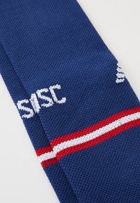 Mörkblå stickad halsduk med texturerad väv, som har vit text och en röd- och vitrandig detalj.
