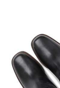 Bottes en cuir noir avec une texture lisse, bout rond et surpiqûres marron contrastantes le long du bord. Design simple, sans quincaillerie supplémentaire.