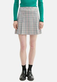 Plissierter Minirock aus Stoff mit einem karierten Muster in Blau, Pink und Weiß. Kombiniert mit einem grünen Oberteil und schwarzen Schuhen.