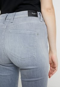 Šedé džínové kalhoty z denimu s úzkým střihem, s černou koženou nášivkou na zadním pasu a ozdobným prošíváním na zadních kapsách.