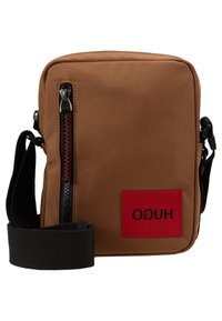 Brązowa kompaktowa torba na ramię z czarnym regulowanym paskiem, pionowym czarnym zamkiem błyskawicznym z czerwonym przeszyciem oraz czerwoną naszywką z logo "HUGO".
