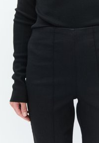 Black ribbed long-sleeve top with fitted silhouette, paired with high-waisted black trousers featuring clean lines and textured fabric.