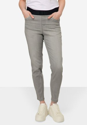 Šedé denimové kalhoty s černým elastickým pasem, slim fit, přední kapsy a hladká textura, doplněné bílými platformovými teniskami.