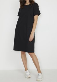 Vestido corto de algodón negro de manga corta con cuello redondo, bolsillos laterales y un ajuste relajado, combinado con zapatillas blancas.