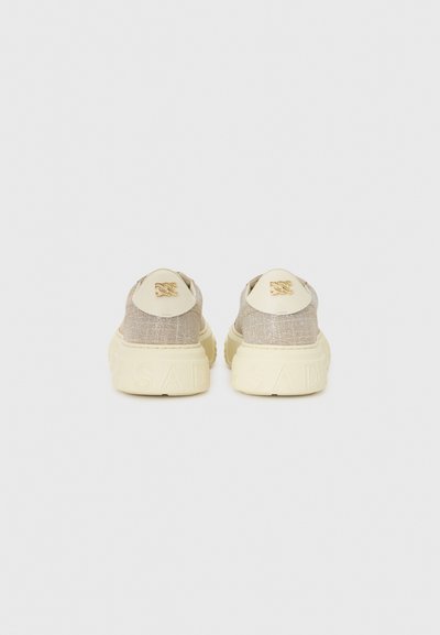 Baskets en tricot beige avec une finition texturée et des semelles crème. Présente un détail de logo à l'arrière et des coutures le long du talon.