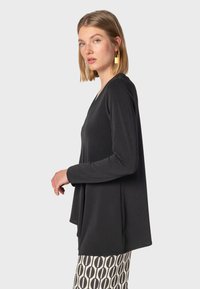 Svart långärmad topp med V-ringning, tillverkad av mjukt tyg. Silhuetten är lös passform och kombineras med mönstrade byxor.