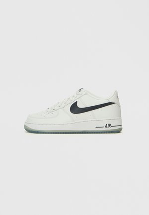Nike Air Force 1 αθλητικά παπούτσια, με λευκό δερμάτινο άνω μέρος, μαύρο λογότυπο Swoosh, στρογγυλή μύτη και διάφανο καουτσούκ σόλα.