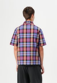 Short-sleeve, collared shirt with a multicolored plaid pattern in purple, pink, brown, and blue. Cotton fabric, relaxed fit, and straight hem.