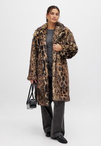 Leopardenmuster-Faux-Fur-Mantel mit einem breiten Kragen und Knöpfen, getragen über einem grauen Oberteil und grauen Cordhosen, kombiniert mit einer schwarzen Handtasche.