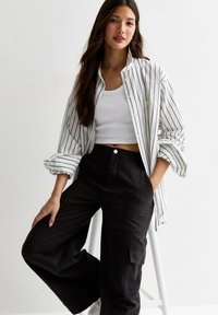 Randig skjorta med knappar i vitt och marinblått, bärs över en vit linne. Matchas med högmidjade, svarta cargobyxor. Avslappnad, lager-på-lager-look.