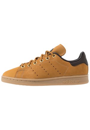 Brun Adidas lavt snørsko med guldøjne, perforerede sidelister, sort hælflap og gummisål.