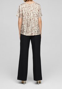 Blusa a maniche corte beige con motivo a pois marroni, abbinata a pantaloni neri a gamba larga. Tessuto liscio con una vestibilità rilassata.