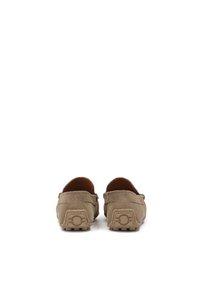 Taupe színű velúr mokaszin, lekerekített orral, slip-on kialakítással és texturált gumitalppal, amelyen kör alakú akcentus található a saroknál.