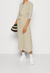 Raidalline mekko beige ja ruskeana, jossa on kaulus, kolmannekselle hihat, sitominen vyö ja lentävä hame. Yhdistetty valkoisiin tennareihin.