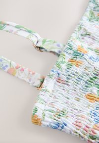 Borsa con motivo floreale su base bianca, caratterizzata da una texture arricciata, tracolle regolabili e dettagli in metallo dorato.