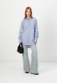 Prugasta modra srajca z dolgimi rokavi, v kombinaciji s svetlimi flare jeans hlačami in majhno črno torbico, ki ima teksturiran dizajn.