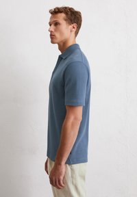 Polo a maniche corte in tessuto blu texturizzato con colletto classico, caratterizzato da un'accentuazione sul lato dell'orlo e vestibilità rilassata.