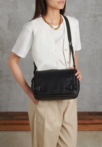 Schwarze Leder-Crossbody-Tasche mit glatter Textur, Reißverschluss und silbernen Hardware-Akzenten. Rechteckige Form mit verstellbarem Tragegurt.