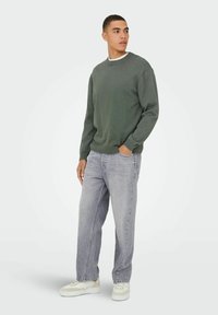 Donkergroen sweatshirt, geribbelde manchetten en zoom, gecombineerd met lichtgrijze jeans. Casual witte sneakers maken de outfit compleet. Eenvoudige en relaxed fit.