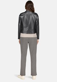 Czarna kurtka ze sztucznej skóry w połączeniu z beżową bluzką i wzorzystymi szarymi spodniami. Kurtka ma dopasowany fason z eleganckimi liniami i stojącym kołnierzem.